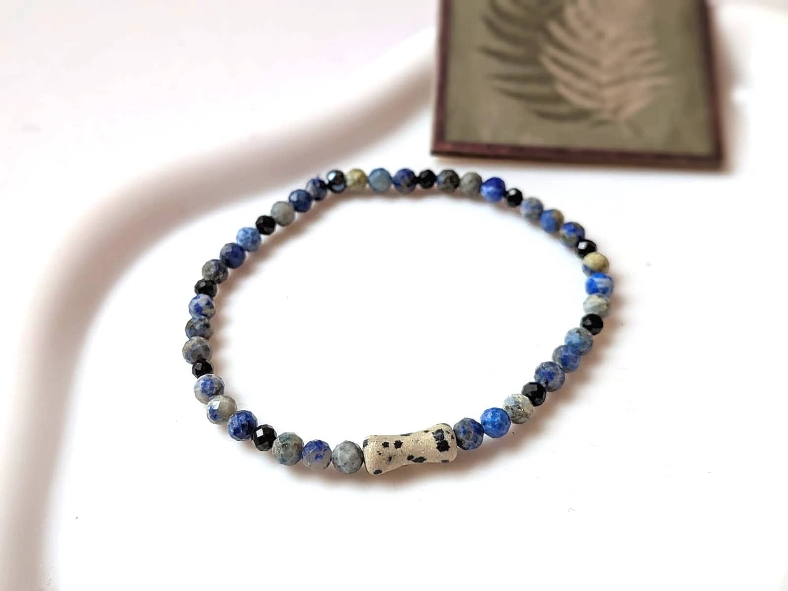 Lapis lazuli i jaspis dalmatyński. Drobne granatowe i szare kulki przeplatają się z jasnymi, nakrapianymi bryłkami. Złociste przekładki dodają delikatnego połysku. Ujęcie 1.